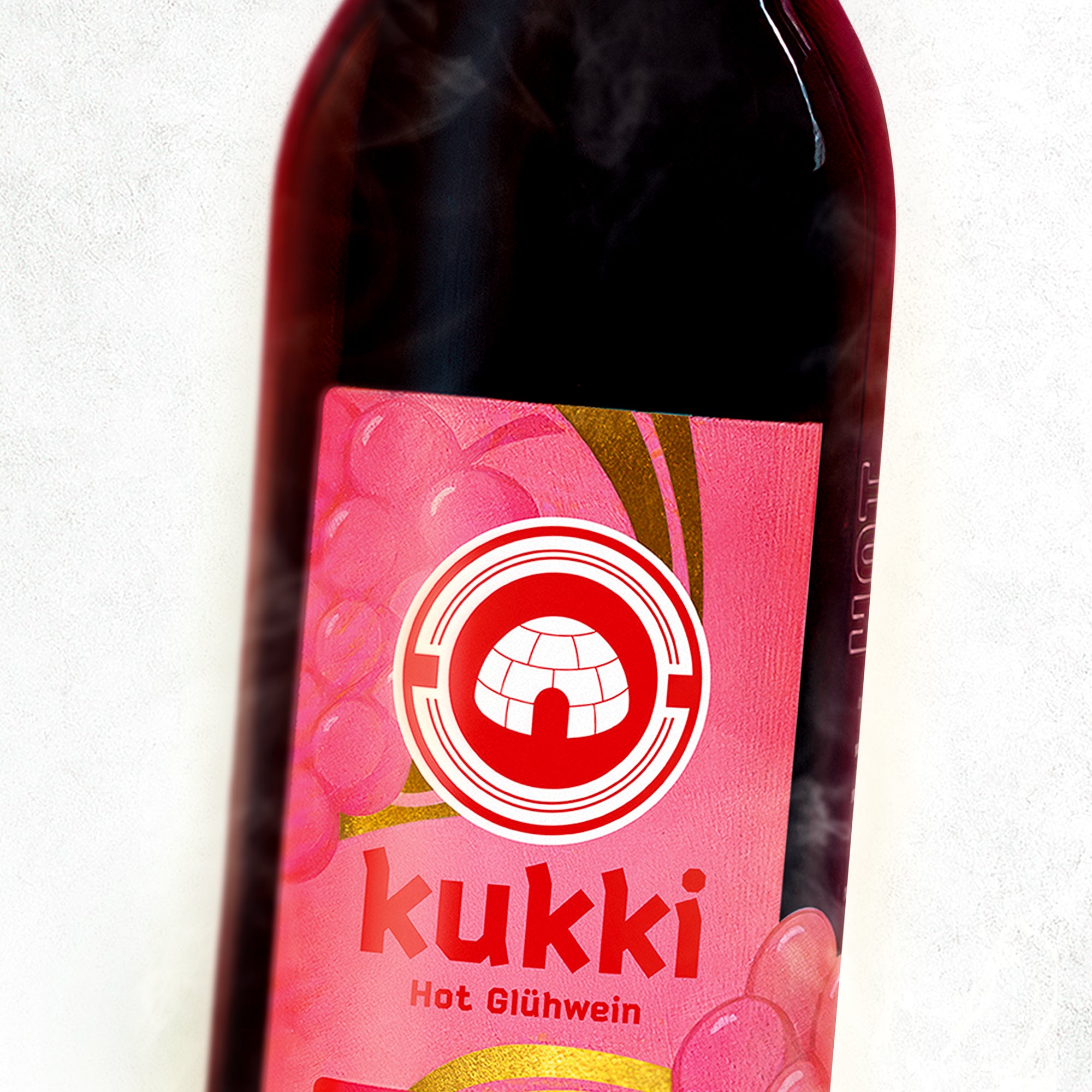 Dunkle Glasflasche mit kukki Cocktail Label für Hot Glühwein und pinken Weintraubenmotiven auf festlichem Etikett.