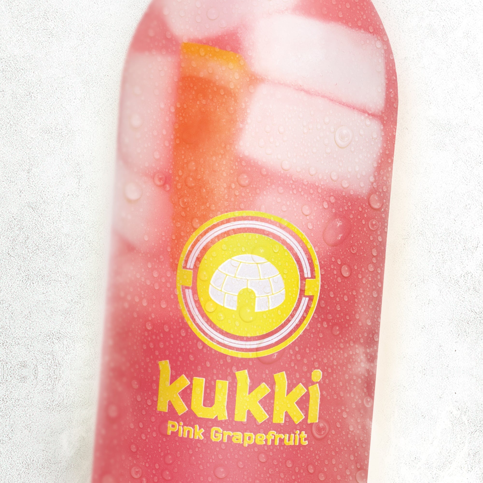 Eingefrorener kukki Cocktail Pink Grapefruit mit Eiswürfeln in Glasflasche vor weißem Hintergrund.