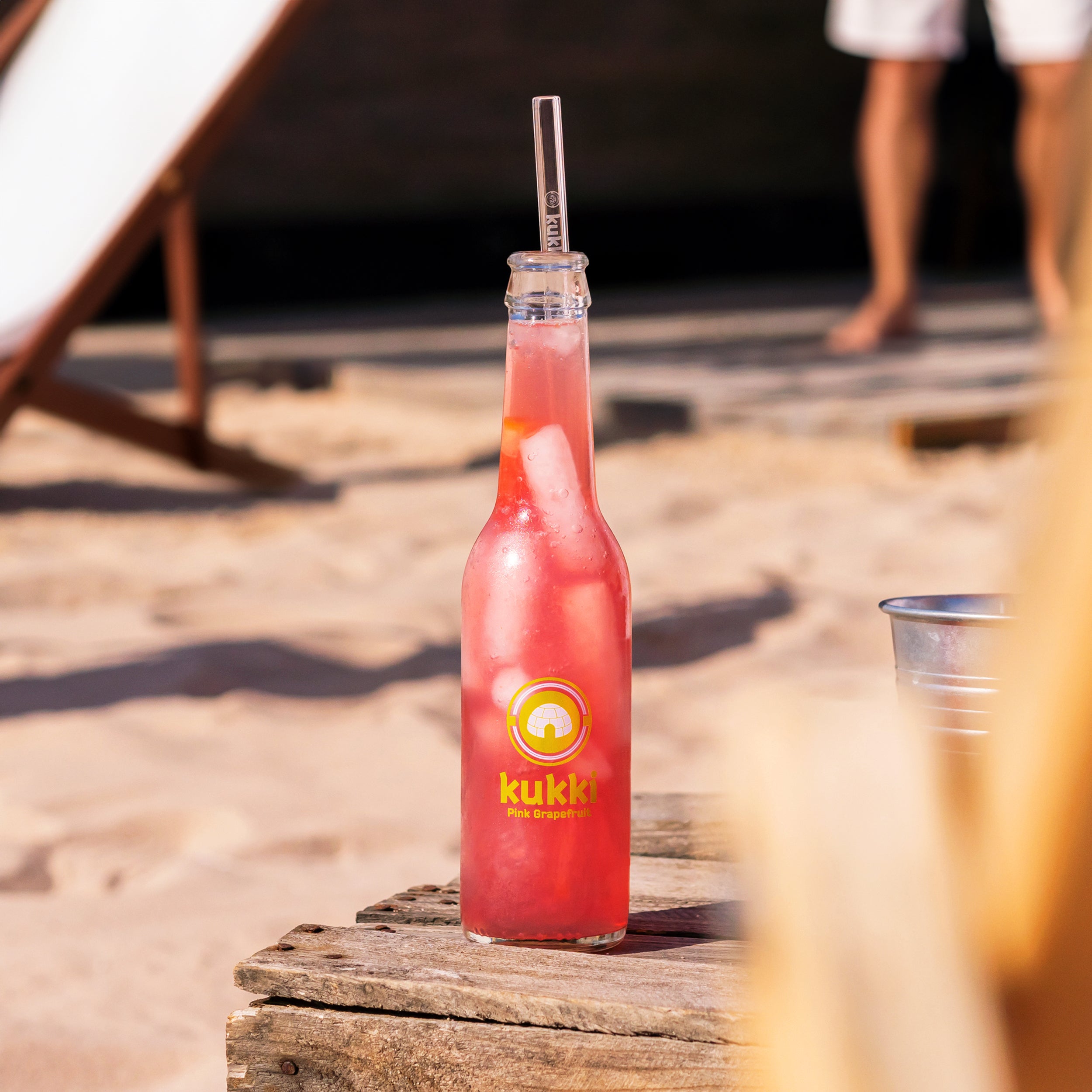 gekühlte kukki cocktail glasflasche pink grapefruit mit eis und strohhalm auf holztisch am sandstrand