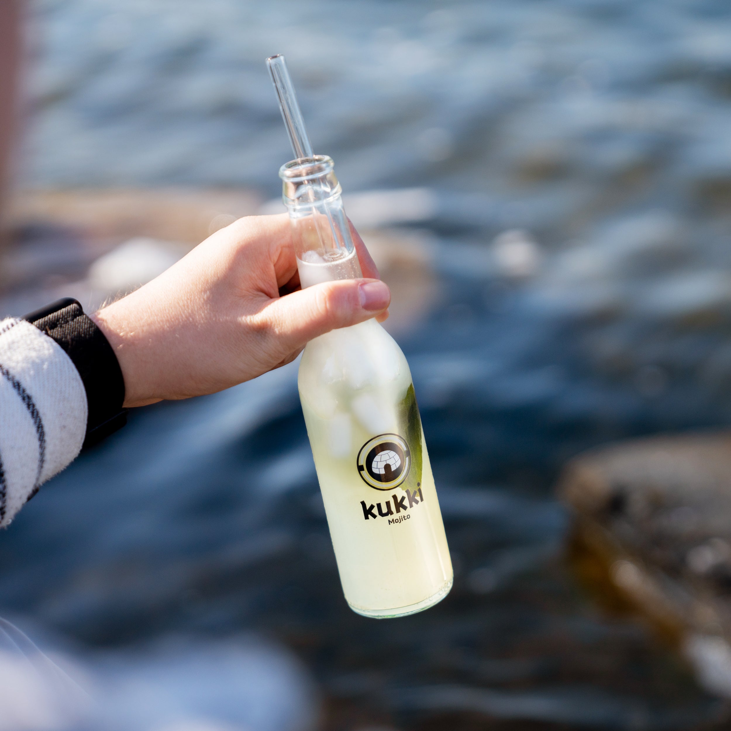 Glasflasche mit hellem grünen kukki Cocktail Mojito, Eiswürfeln und Minzblatt vor Wasserlandschaft