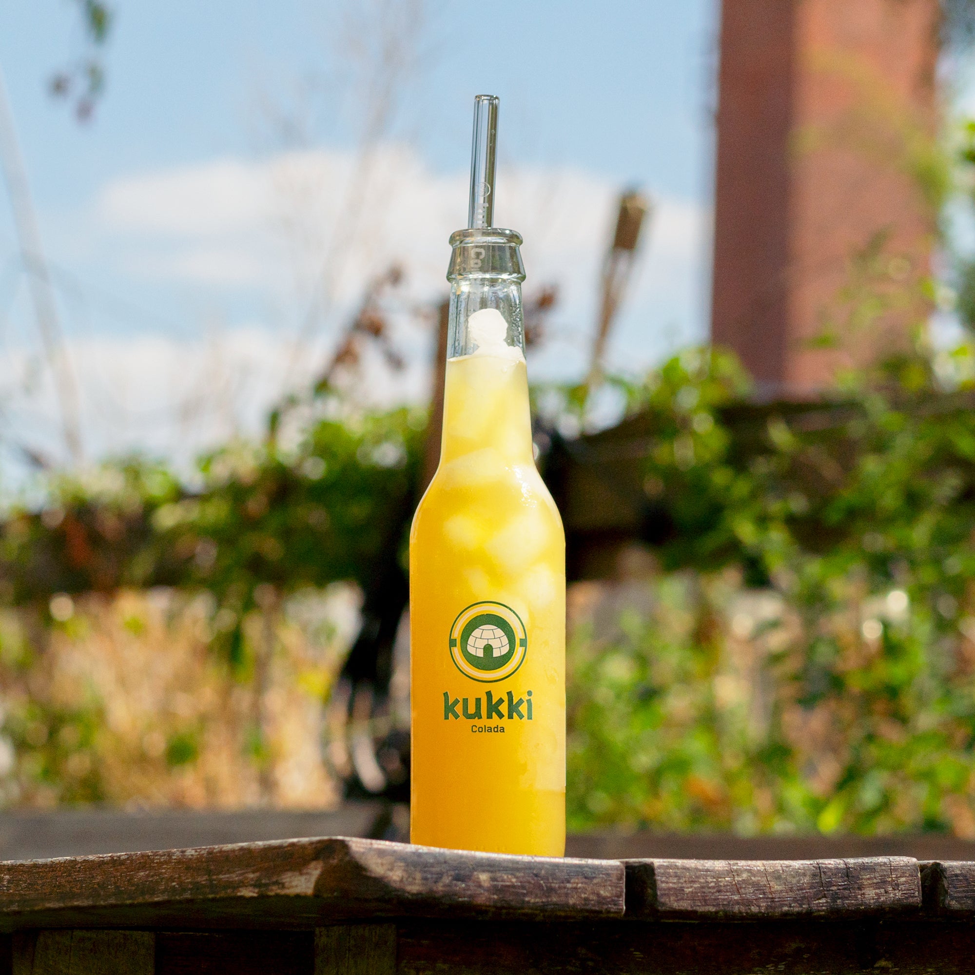 kukki Cocktail Colada in Glasflasche mit gelb-orangefarbenem Eisgetränk auf Holztisch