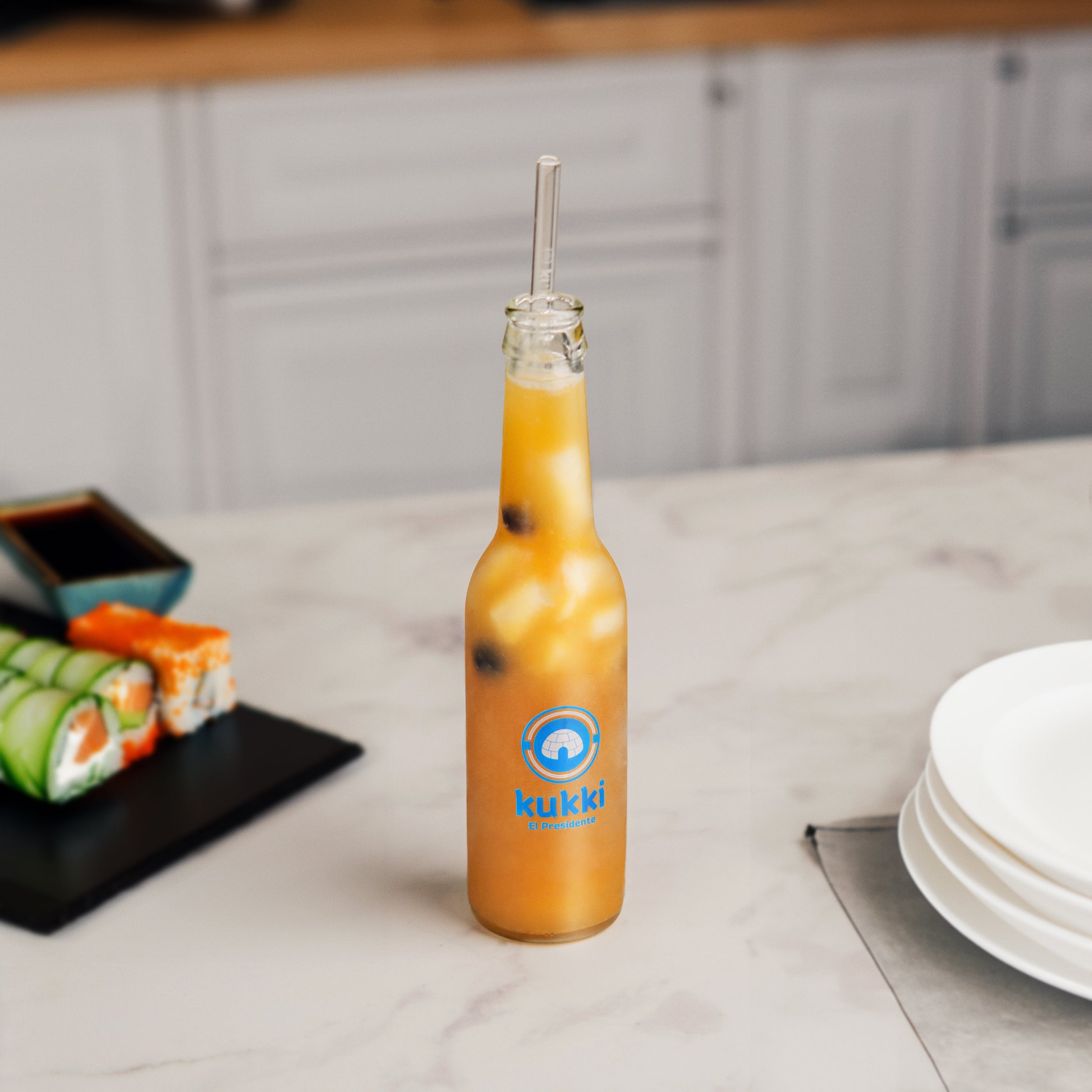 kukki Cocktail El Presidente im Glas mit Eis und schwarzen Tapiokaperlen auf Marmoroberfläche neben Sushi und weißem Tellerstapel in moderner Küche