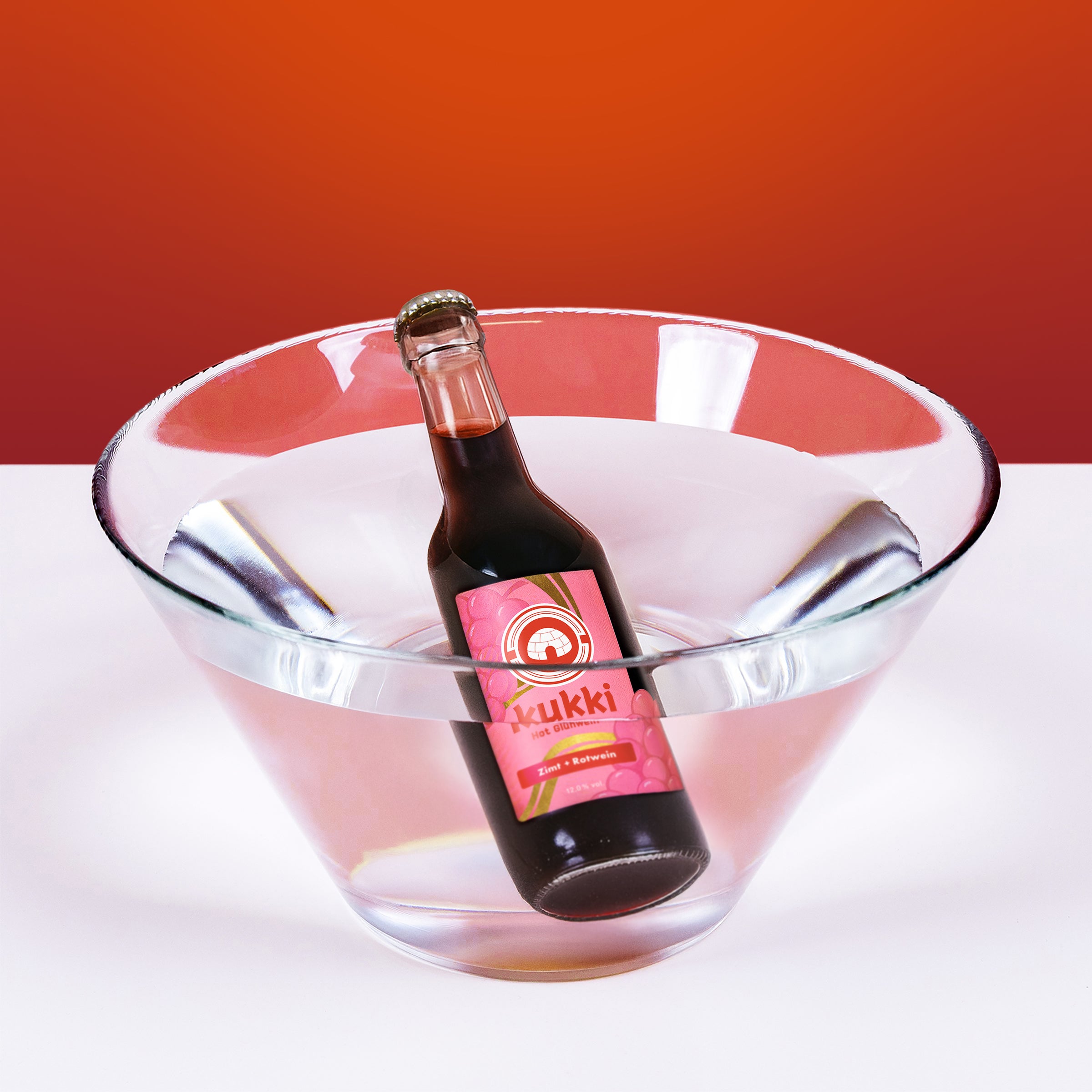 Dunkle Glasflasche kukki Cocktail Glühwein im Wasser, vor rotem Hintergrund.