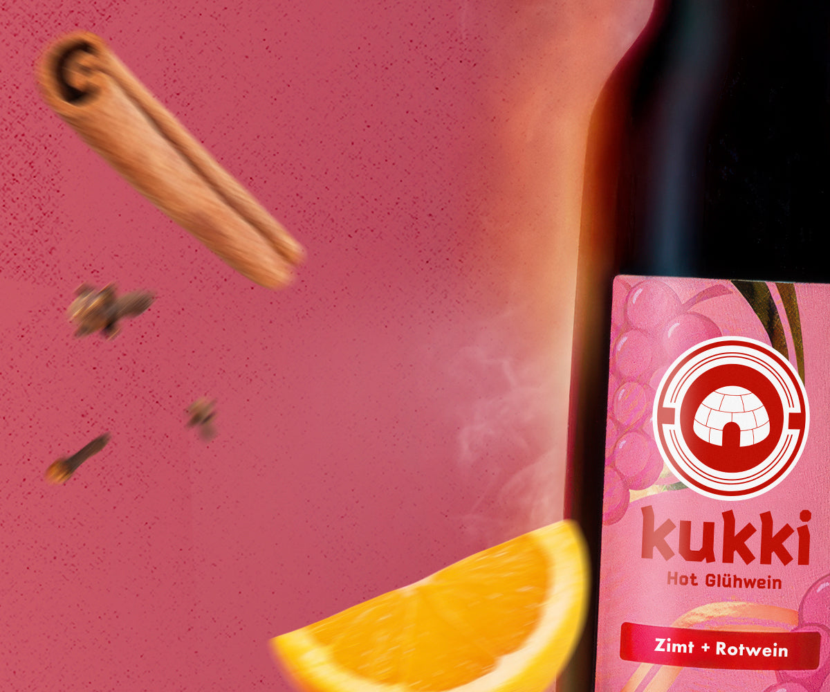 kukki Cocktail Hot Glühwein in Glasflasche mit Orangenscheibe und Gewürzen auf rosa Hintergrund