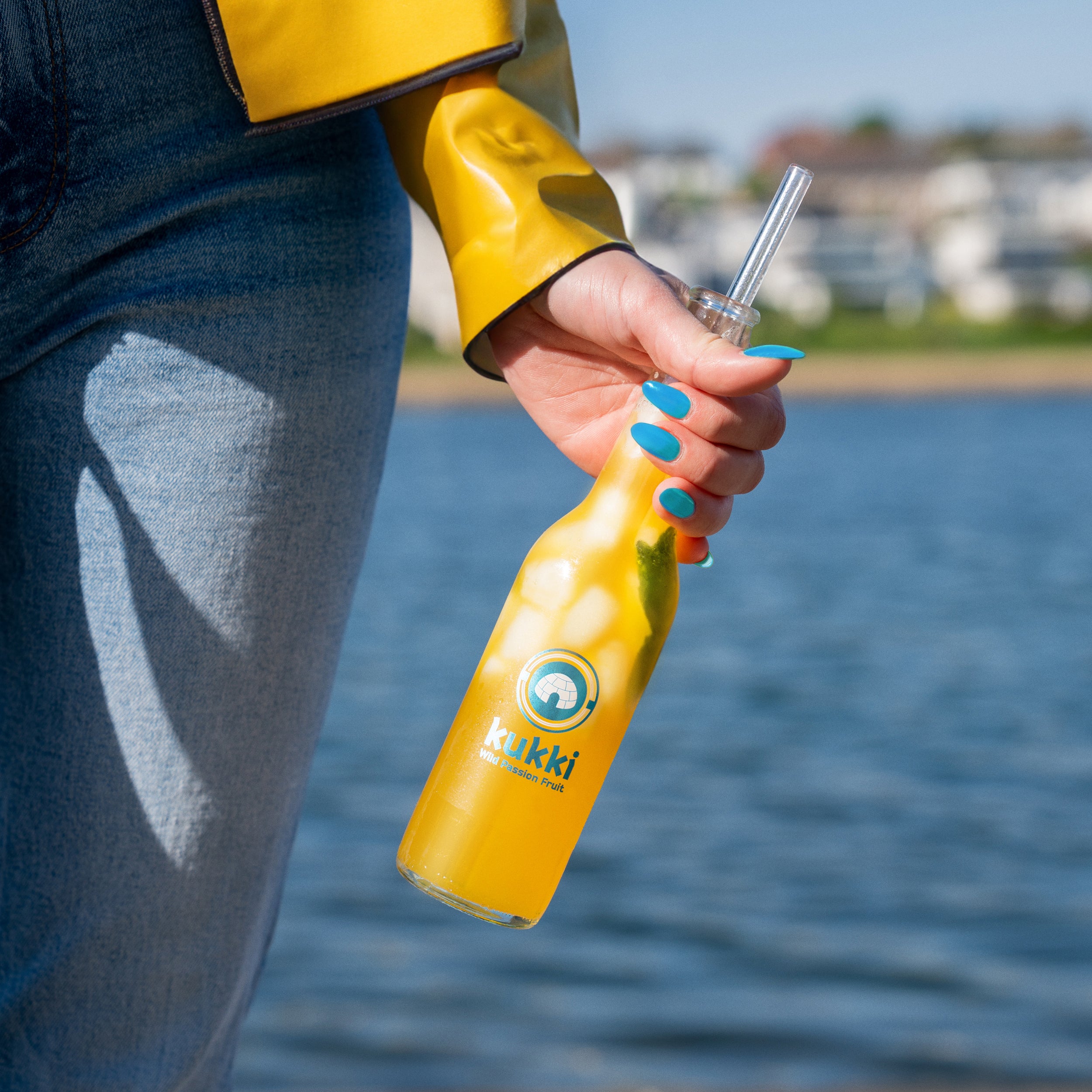 kukki Cocktail Wild Passion Fruit Glasflasche mit Eis und grünem Blatt in Hand vor Wasser