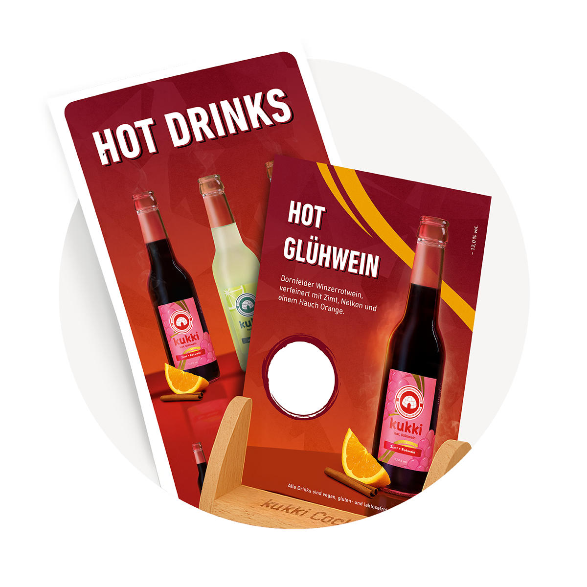 Zwei kukki Cocktail Hot-Drink-Karten mit Glasflaschen, Zimtstangen und Orangenscheiben im Holzhalter auf rotem Hintergrund.