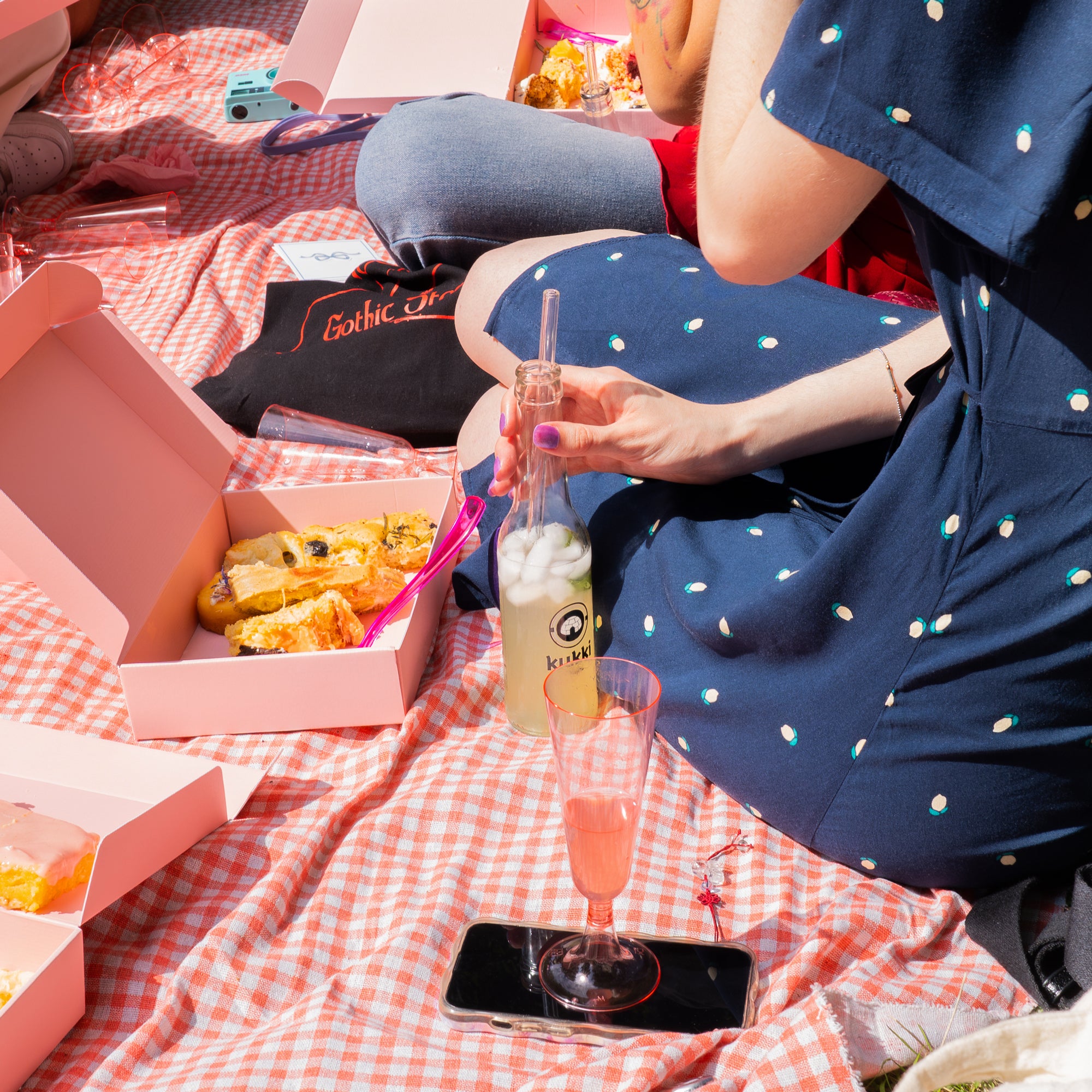 Zwei Personen beim Picknick mit kukki Cocktail in Glasflasche und pinken Gebäckschachteln