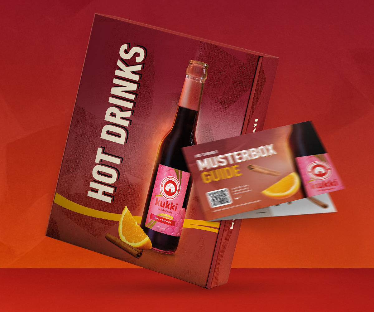 Rote Hot Drinks Musterbox mit kukki Zimt Rotwein Flasche, Orangenscheibe und Zimtstange vor warmem Hintergrund.